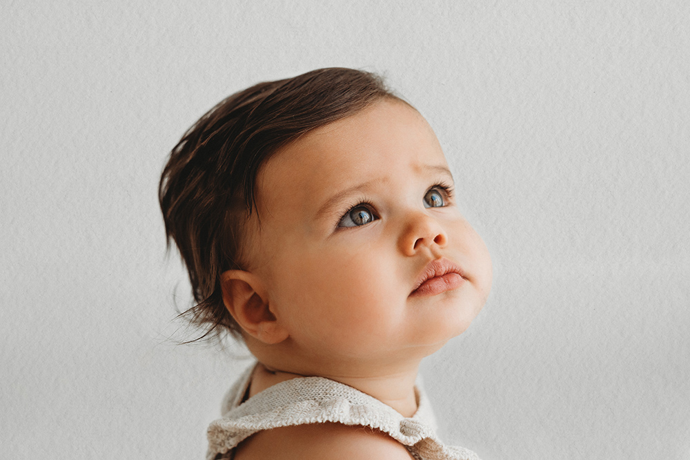 Baby tijdens sittershoot in daglichtstudio zittend en omhoog kijkend.