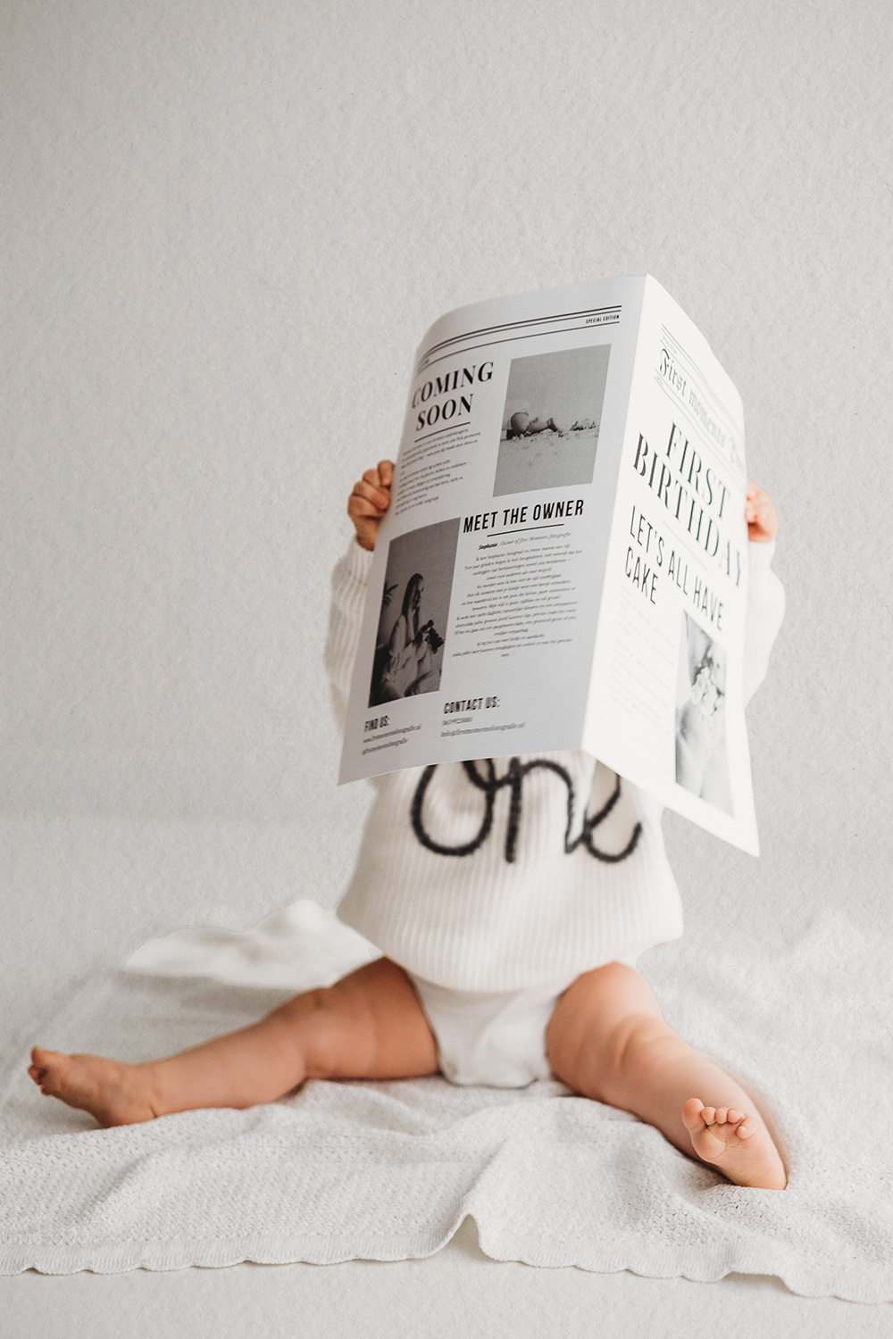 Baby bij een one year shoot leest krantje met "one" trui in daglichtstudio bij cakesmash Limburg.