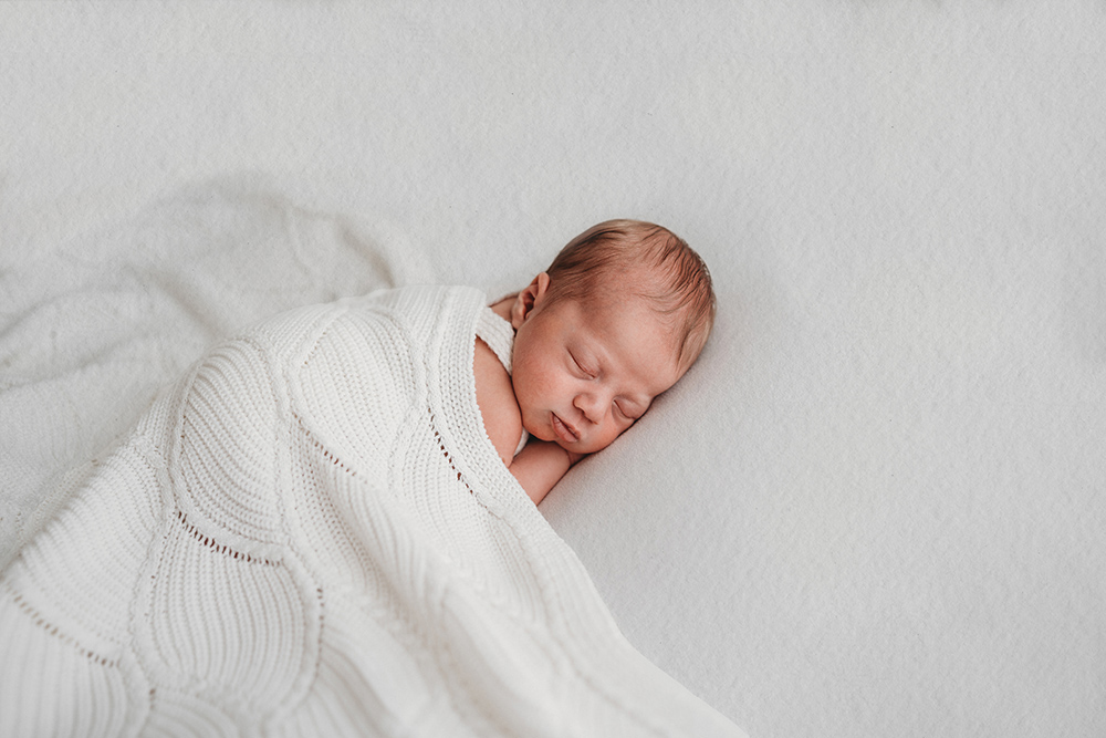Slapende newborn tijdens newbornshoot in Limburg. Baby op lichte achtergrond in daglichtstudio.