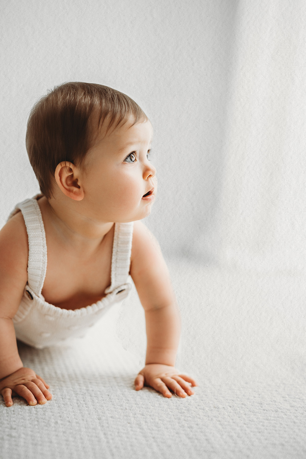 Baby tijdens een sittershoot in daglichtstudio kijkend omhoog op een lichte achtergrond.