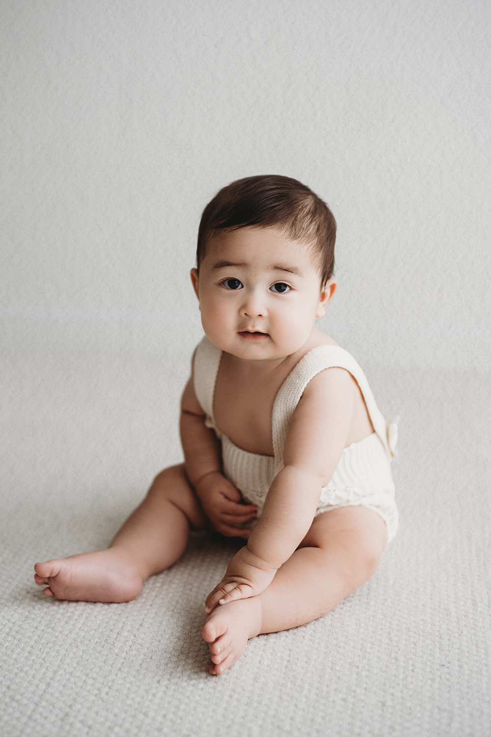 Baby tijdens een sittershoot in daglichtstudio zittend op een lichte achtergrond.