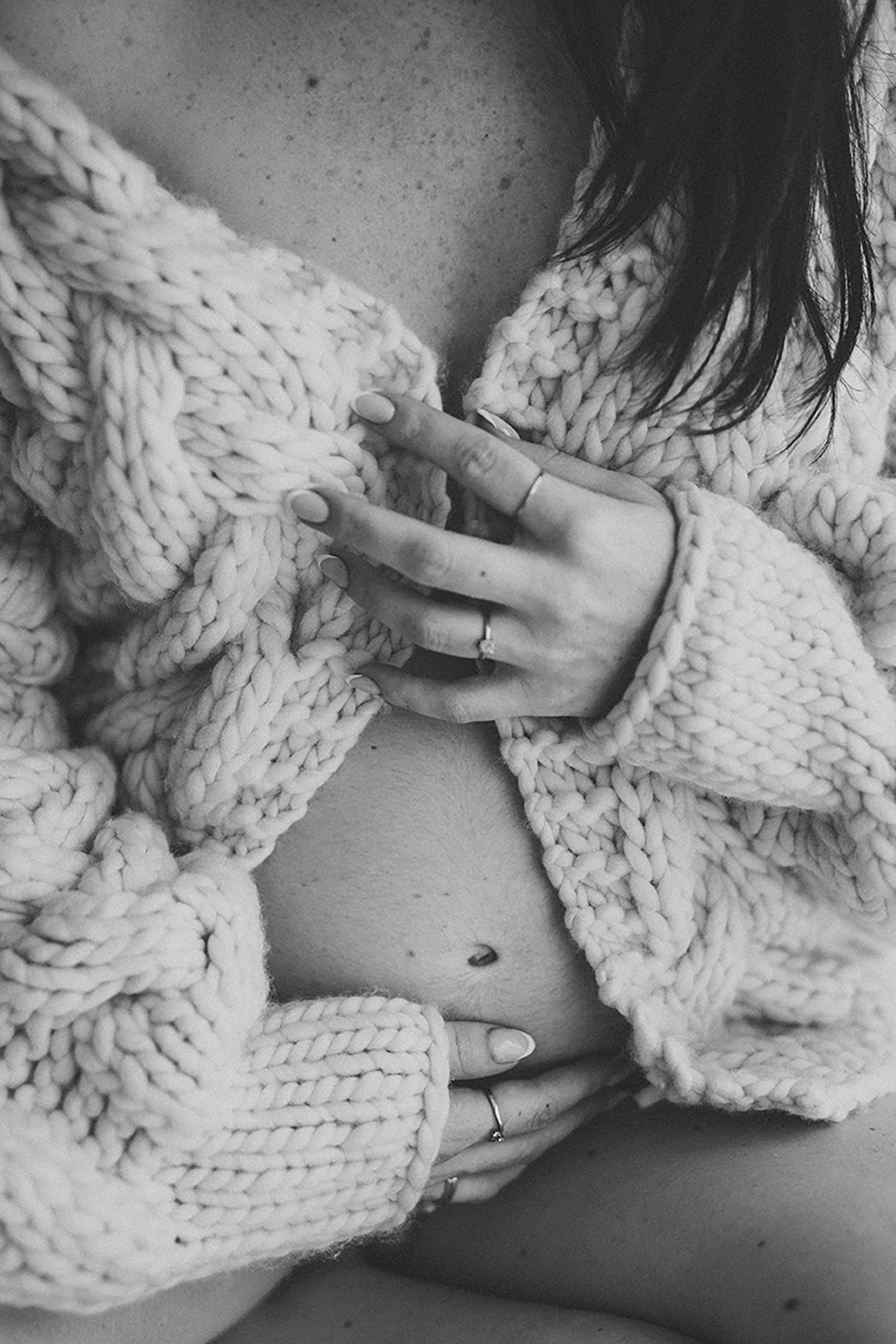 Close-up van zwangere buik tijdens pregnant shoot in daglichtstudio met gebreid vest.